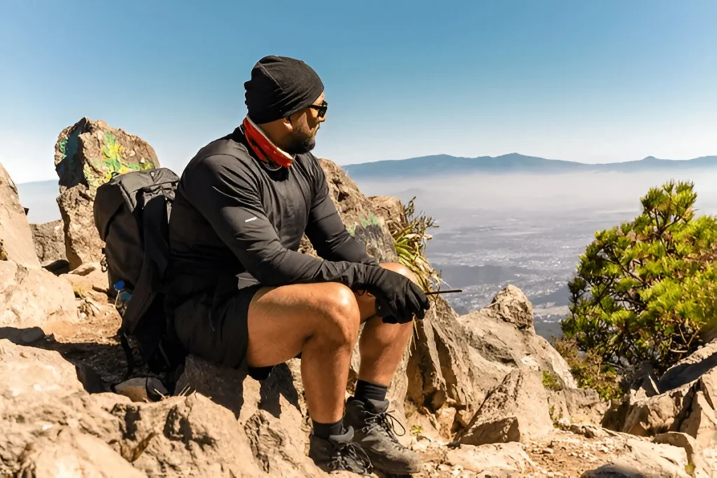 A man in his best hiking gear sits on a rocky mountain summit, overlooking a vast
