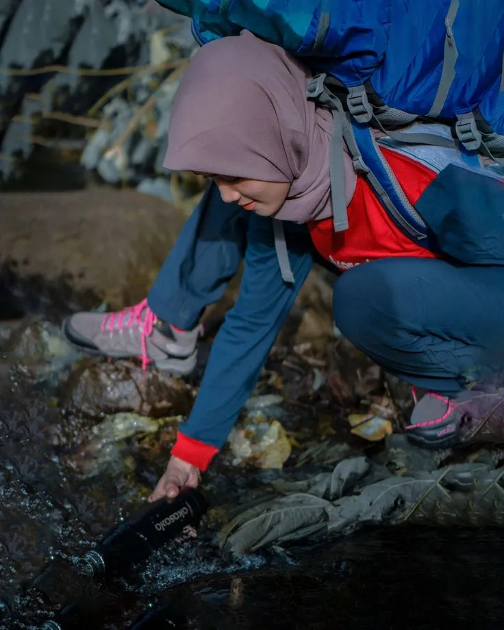 A backpacker fills a water bottle from a stream, illustrating How Much Water to Bring When Backpacking.
