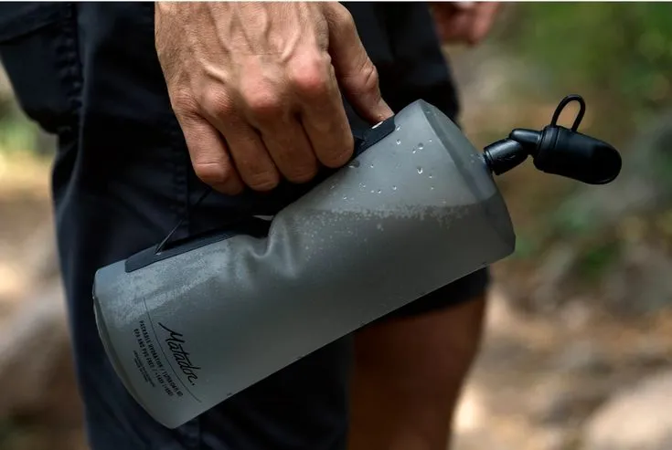 A hiker holding a compact, flexible water bottle—ideal for planning How Much Water to Bring When Backpacking.