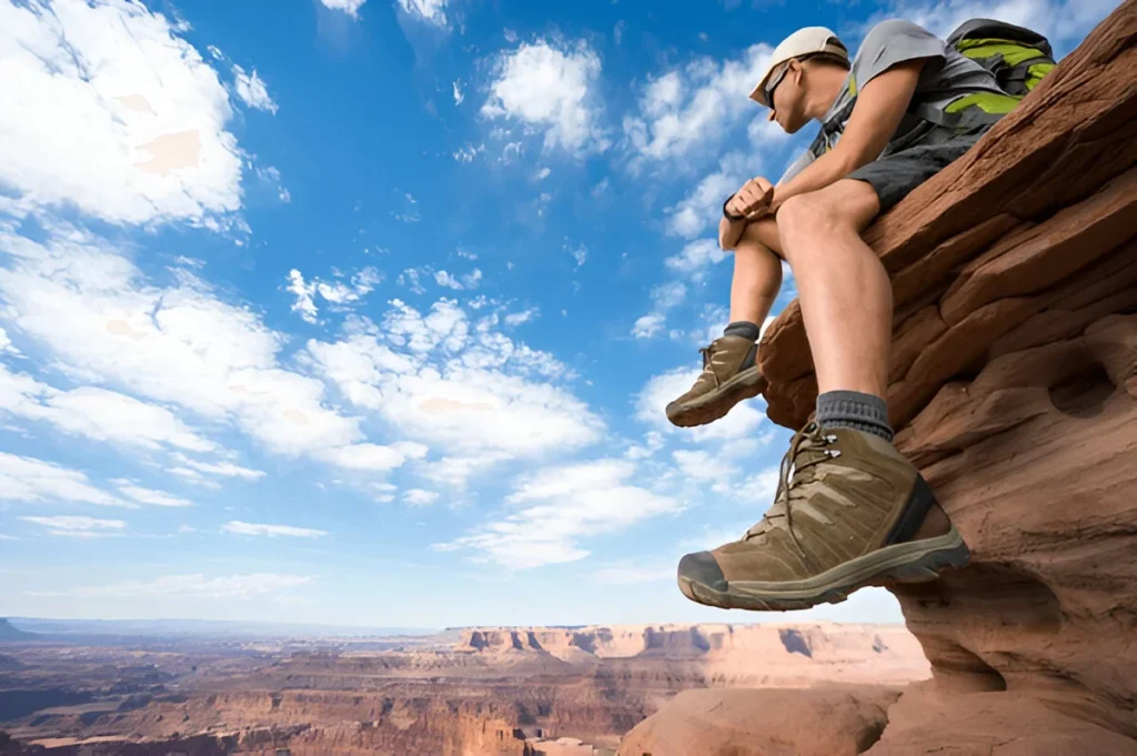 A hiker sitting on a rocky cliff edge wearing durable boots