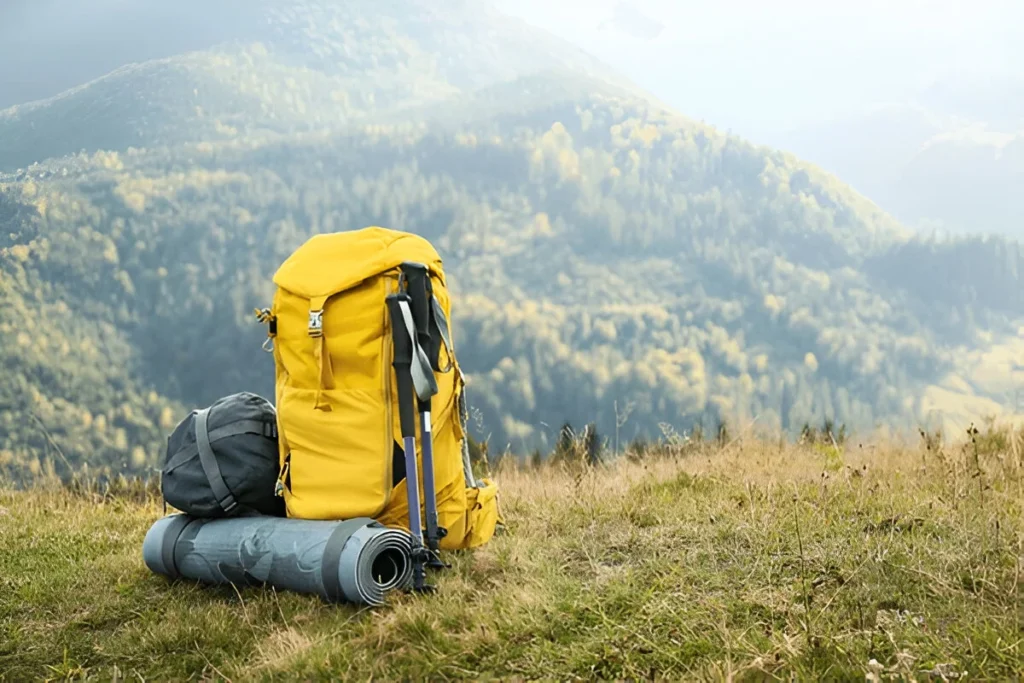 A yellow hiking pack and gear set on a grassy mountain ledge with scenic views, showcasing one of the Best Ultralight Backpacks for outdoor adventures.
