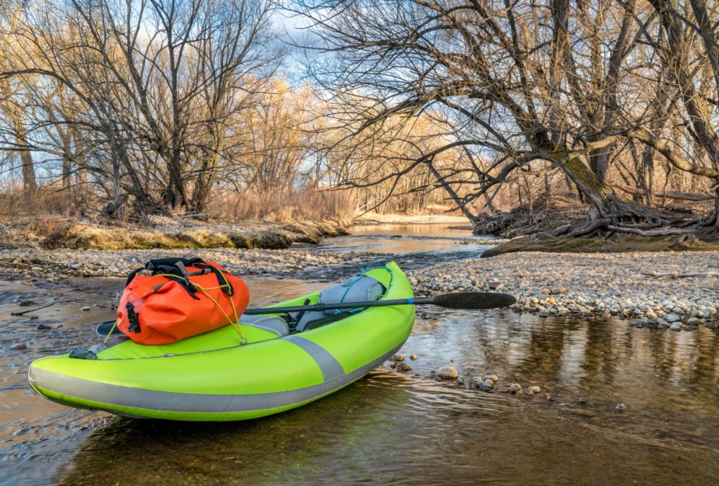 A bright green inflatable kayak with gear rests on a shallow riverbank, highlighting the versatility of the best inflatable kayak for river adventures.