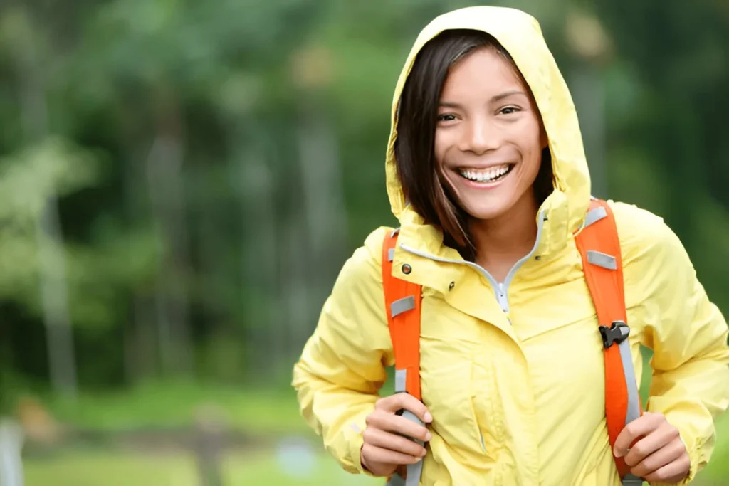 A woman hikes joyfully through the forest in a bright yellow raincoat, perfectly showcasing the best rain jackets for women.
