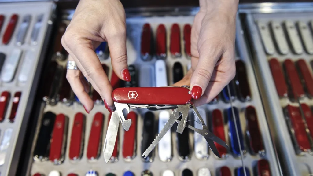 A women holds an open multi-tool in front of a display case filled with red pocket knives, showcasing some of the Best Swiss Army Knives.
