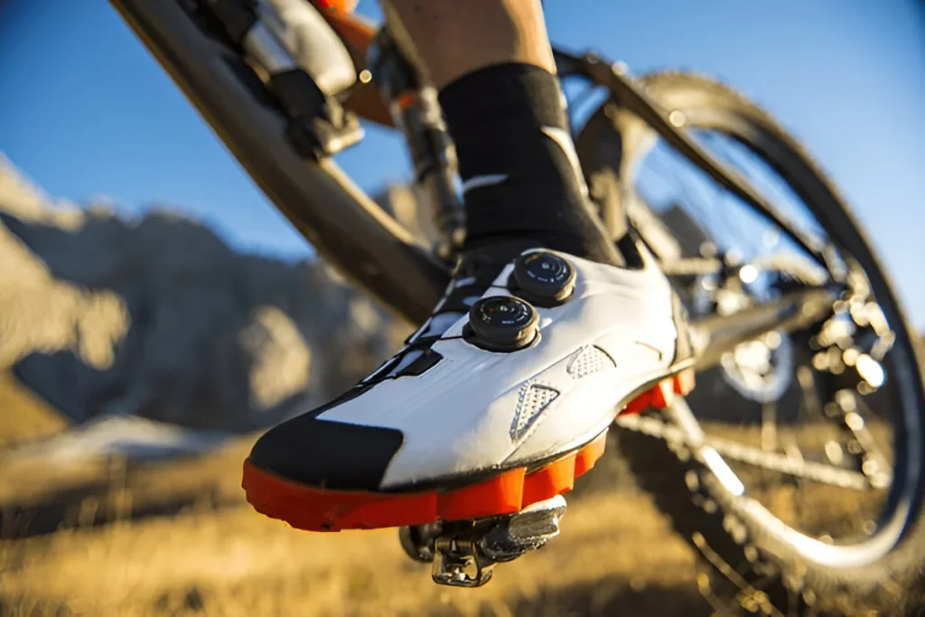 Close-up of a cyclist wearing the best mountain bike shoes with cleats, riding on a rugged trail in the mountains.