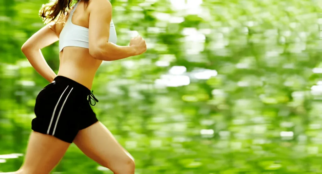 Woman jogging through a green forest wearing the best running shorts for women, designed for comfort and performance.
