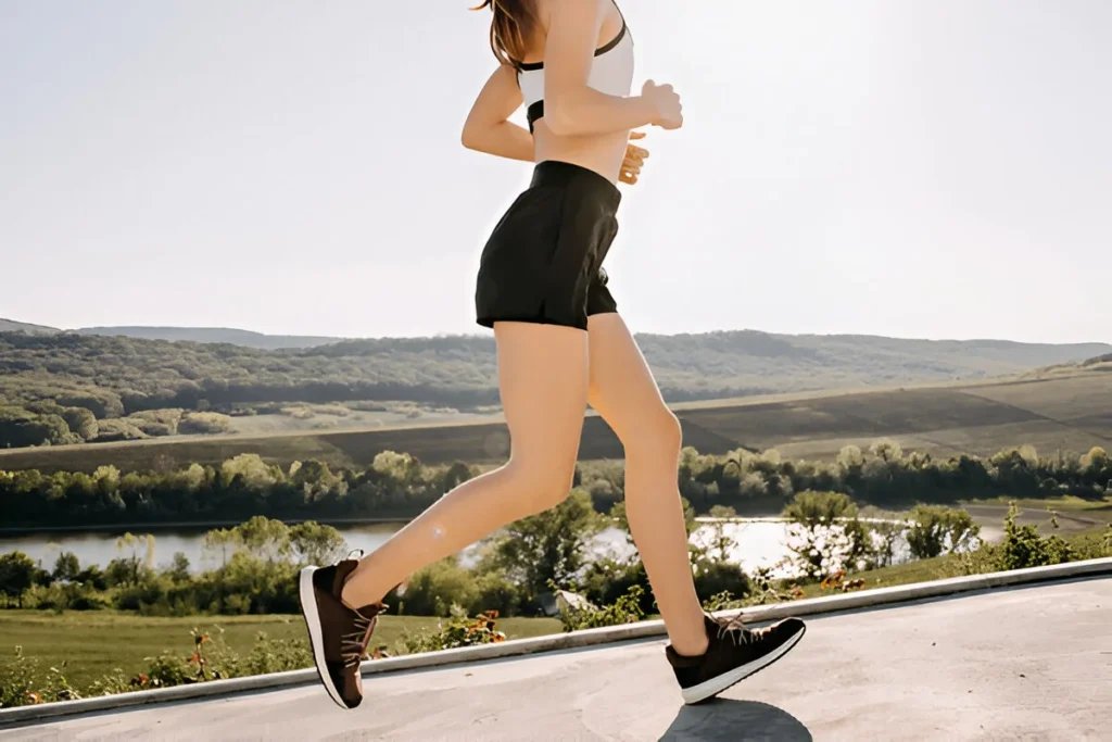 Close-up of woman legs running outdoors on a concrete sidewalk. Sportive girl wearing shorts and a crop top, jogging