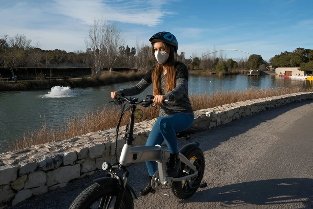 Woman riding one of the best folding electric bikes along a peaceful riverside path on a sunny day.