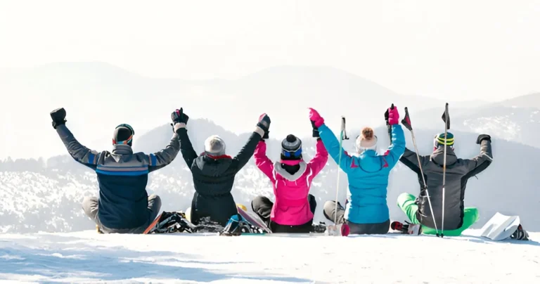 Group of friends in winter gear raising their arms on a snowy mountain, showcasing the Best Ski Jackets for Men in action.