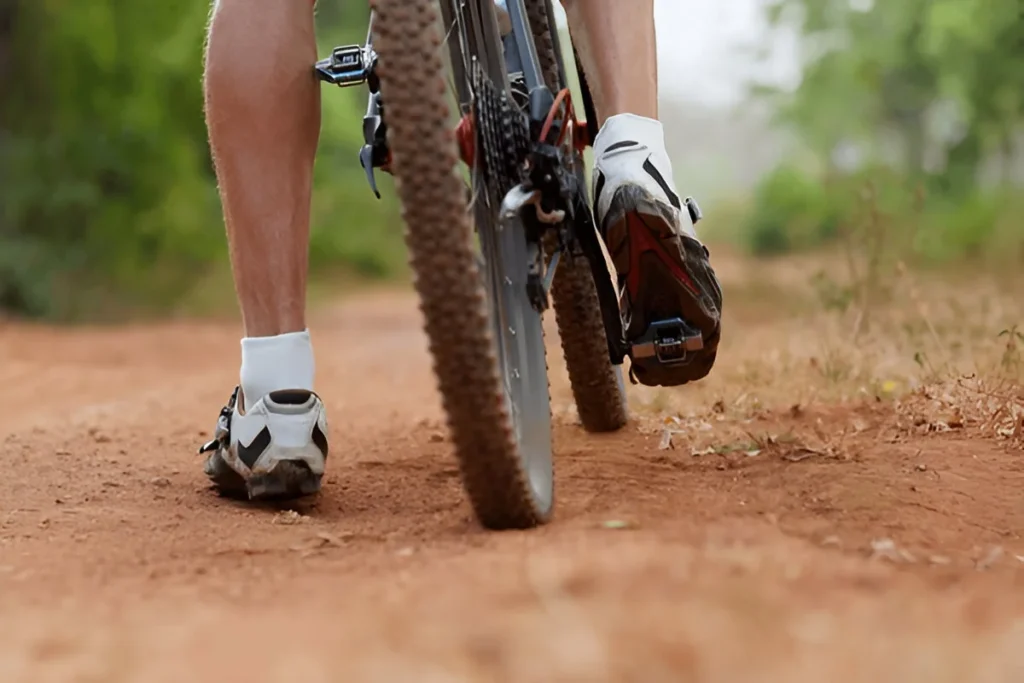 Mountain bike rear wheel and riders foot. Back shot of mountain bike on brown dirt road. Close up view of a Mountain bike tire