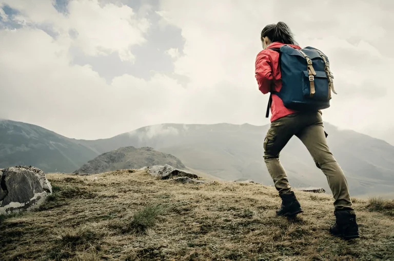 A woman hikes through a rugged mountain trail wearing durable gear, showcasing one of the best hiking pants for women.