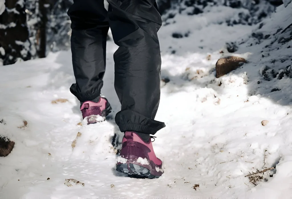 Female hiker on snow covered trail in forest. Winter forest hiking background with proper gear