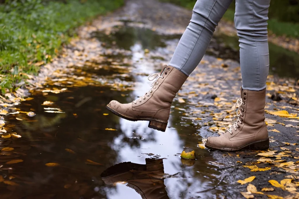 Waterproof leather boots over puddle with reflection. Hiking boot at autumn season. Woman walking on wet footpath after rain