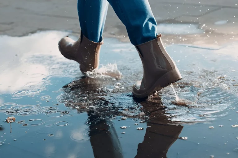 Woman walking through a puddle in rain boots, featured in the Complete Guide to Waterproof Shoes for Women.