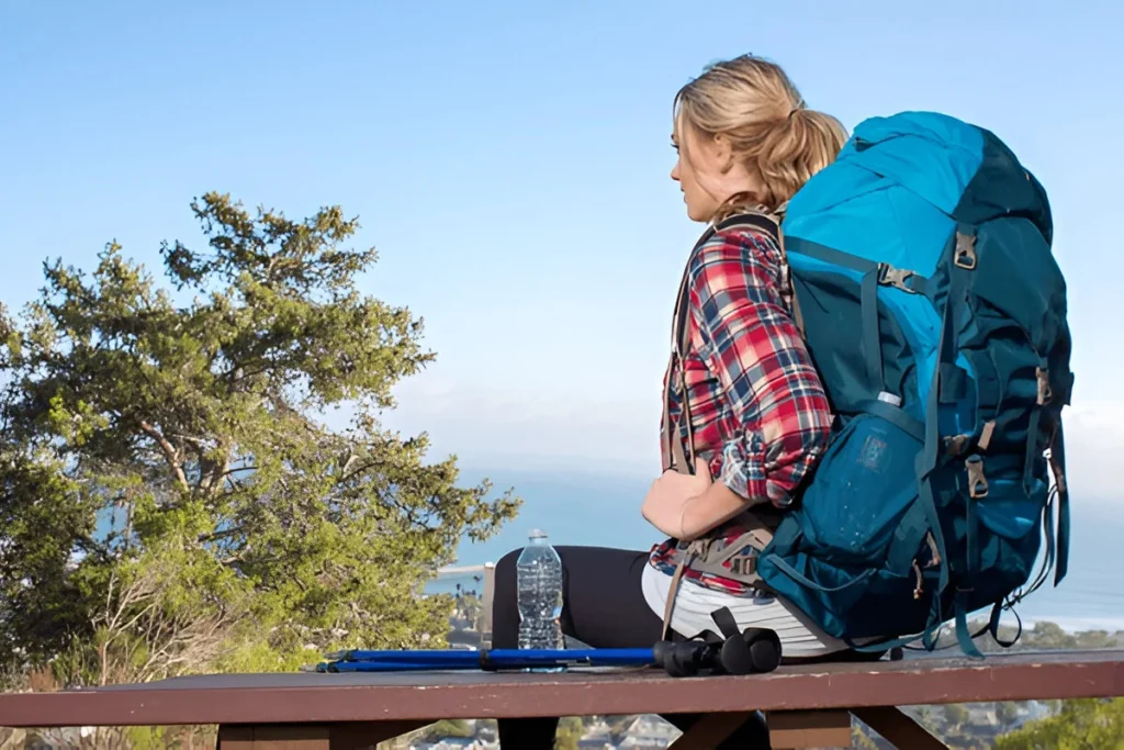A woman with a large blue backpack enjoys a scenic mountain view, highlighting one of the Best Hiking Daypacks for outdoor exploration.