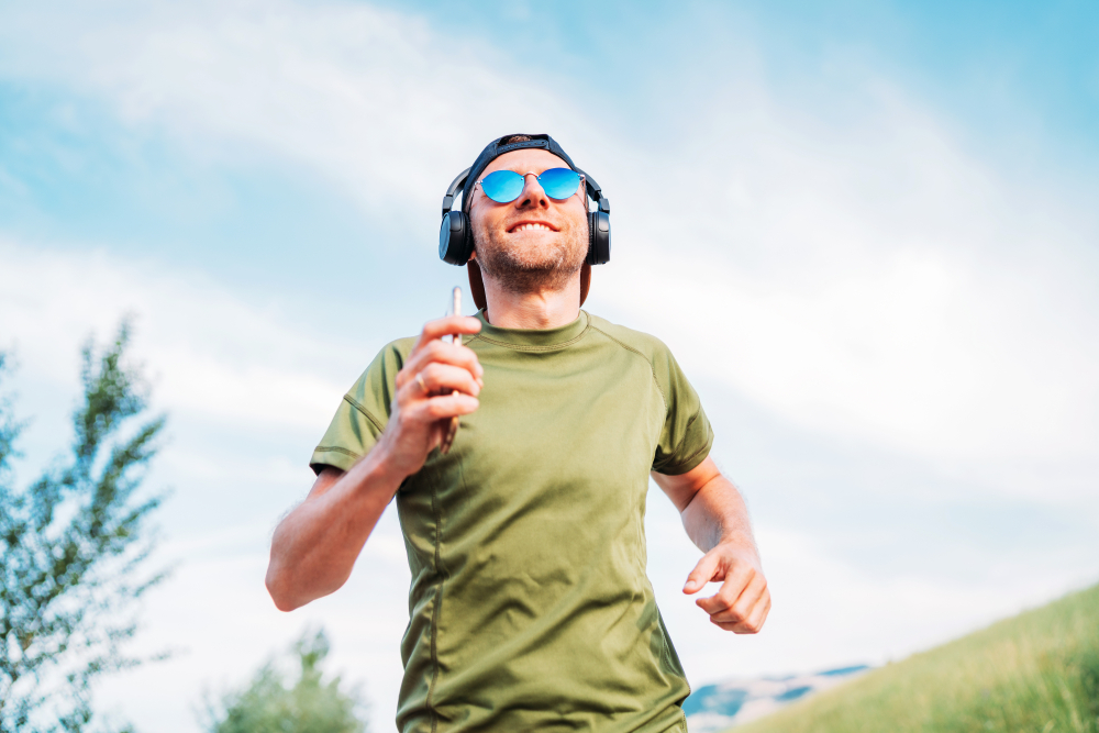 Bearded man in baseball cap, wireless headphones and blue sunglasses cheerful smiling running
