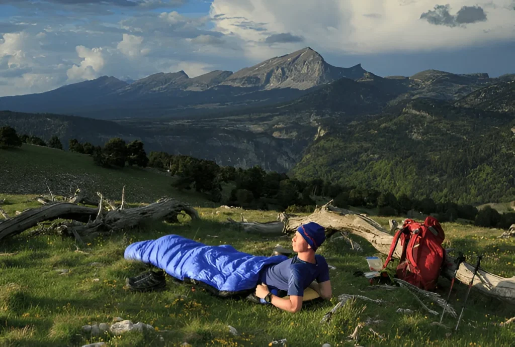 A backpacker relaxes in the mountains wrapped in one of the best backpacking sleeping bags, enjoying comfort and warmth under the open sky.