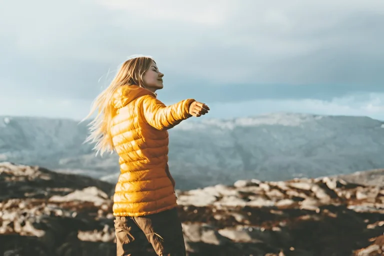 Woman enjoying mountain views in a bright yellow puffer, showcasing the best down jackets for women for outdoor adventures.